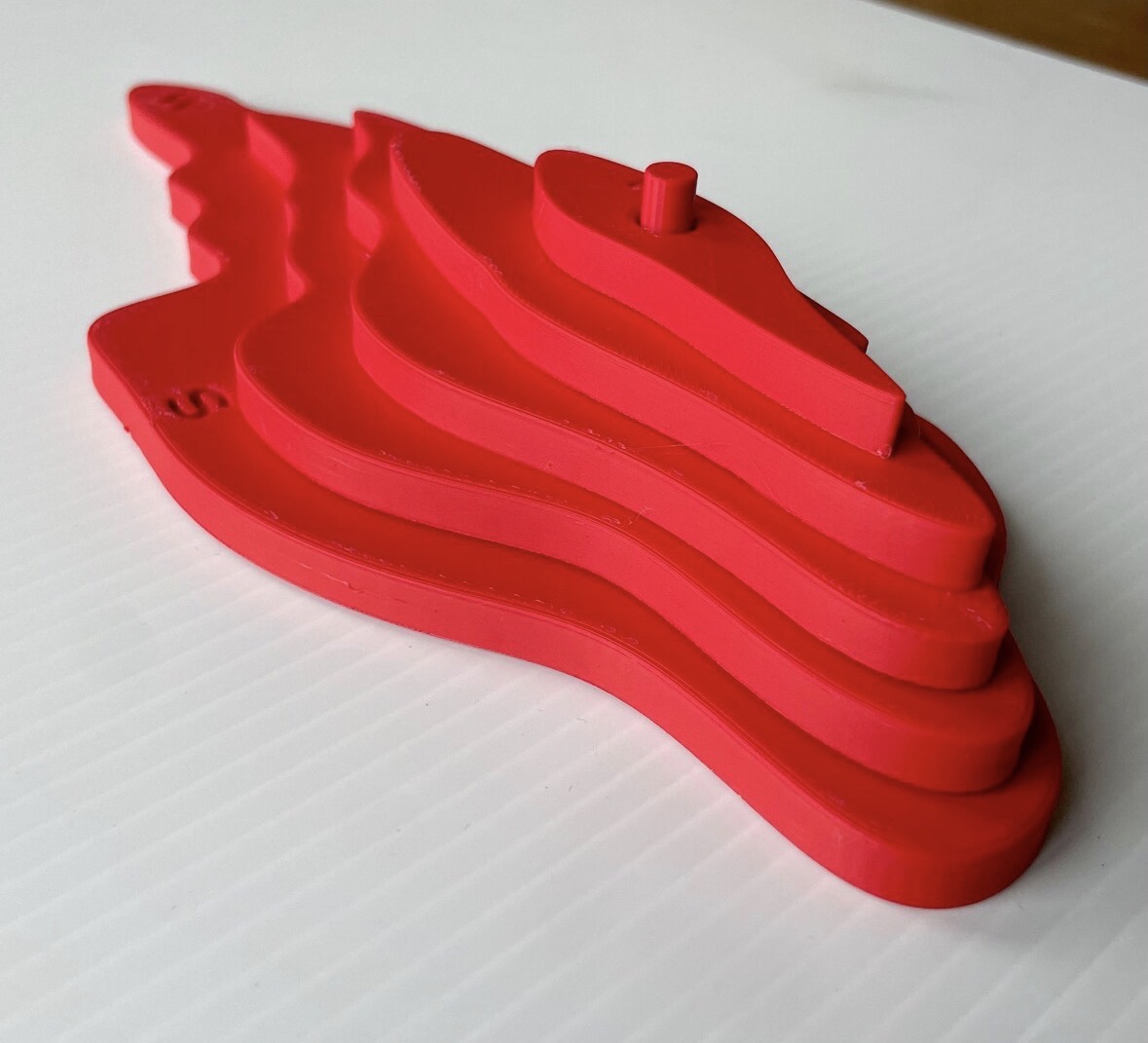 Red 3D topographic map A model assembled from five contour layers with a central alignment peg and debossed compass letters