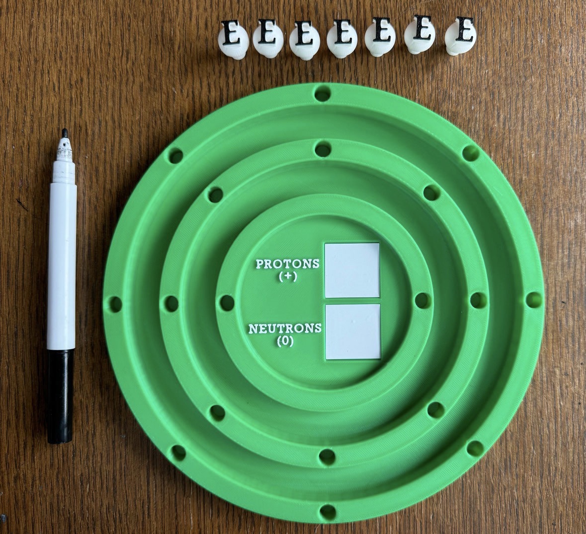 Green Interactive Bohr model with loose electron pegs and a dry-erase nucleus on a wooden desk